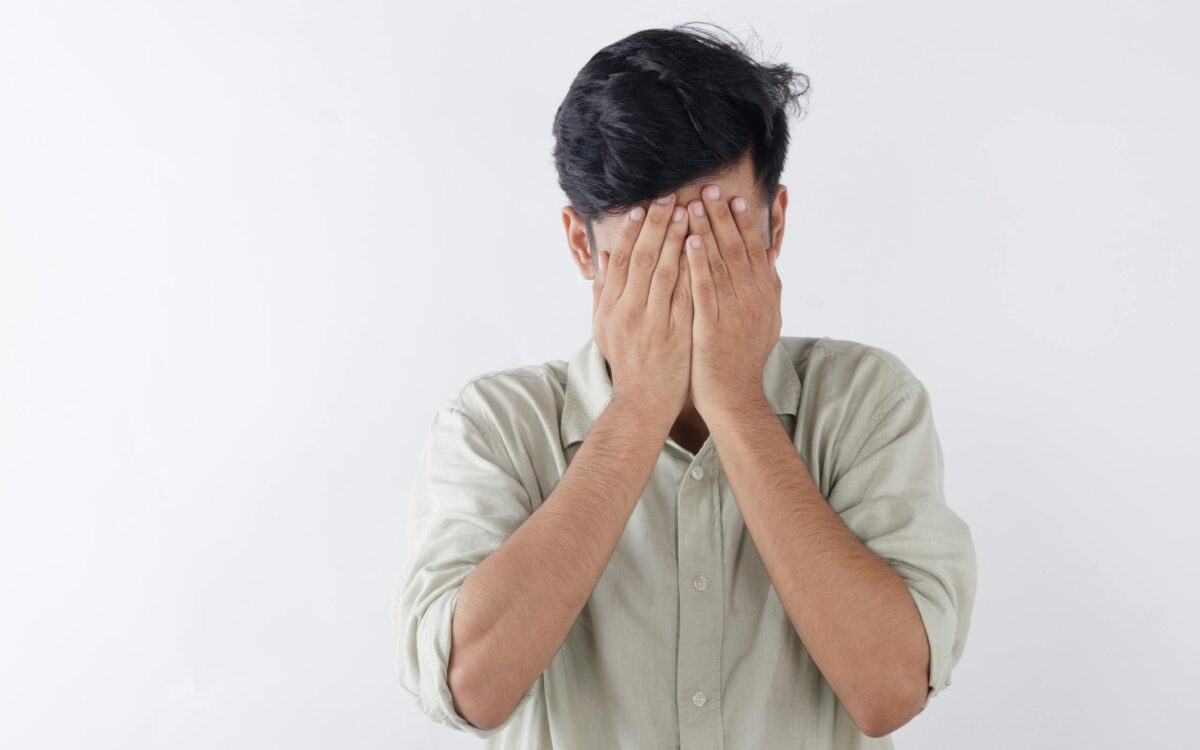 A man covering his face with hands, expressing feelings of stress and emotional struggle.