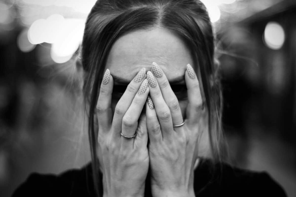 A woman covers her face with hands showing patterned nails, captured in black and white.