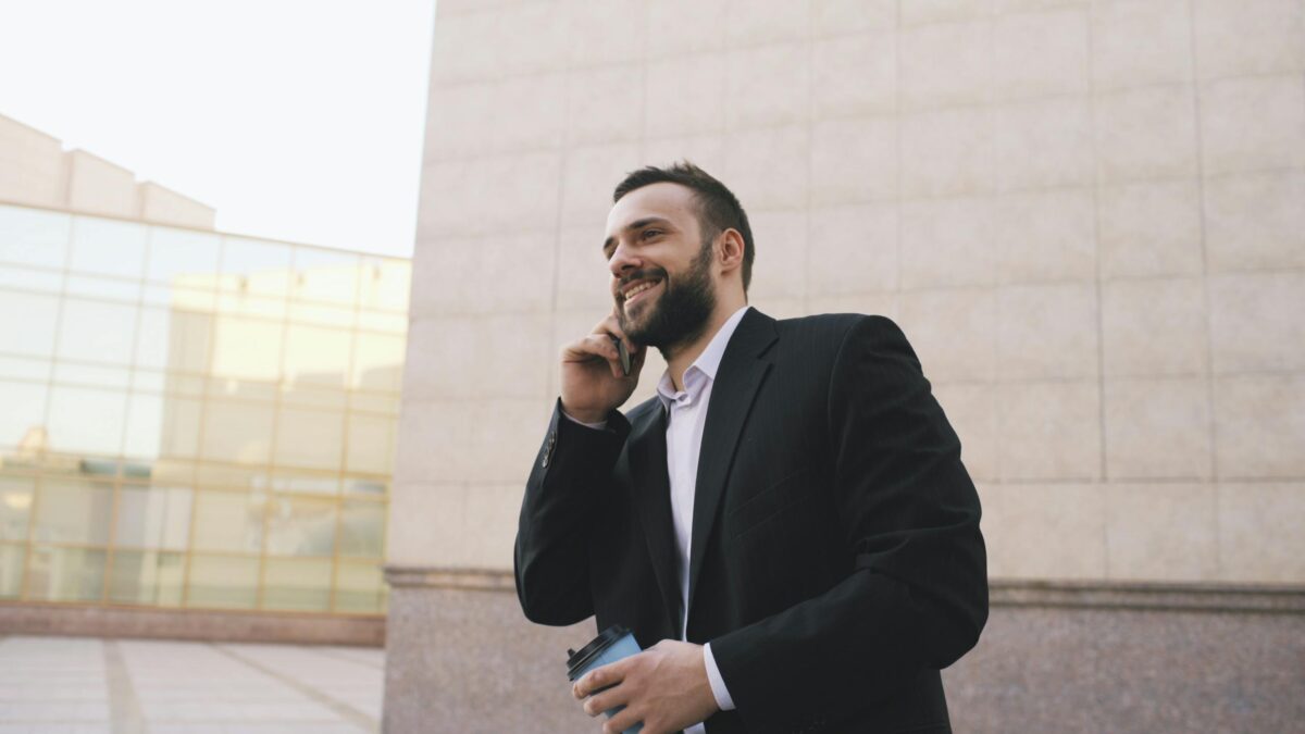 Businessman in suit talking on mobile, holding coffee, urban setting.