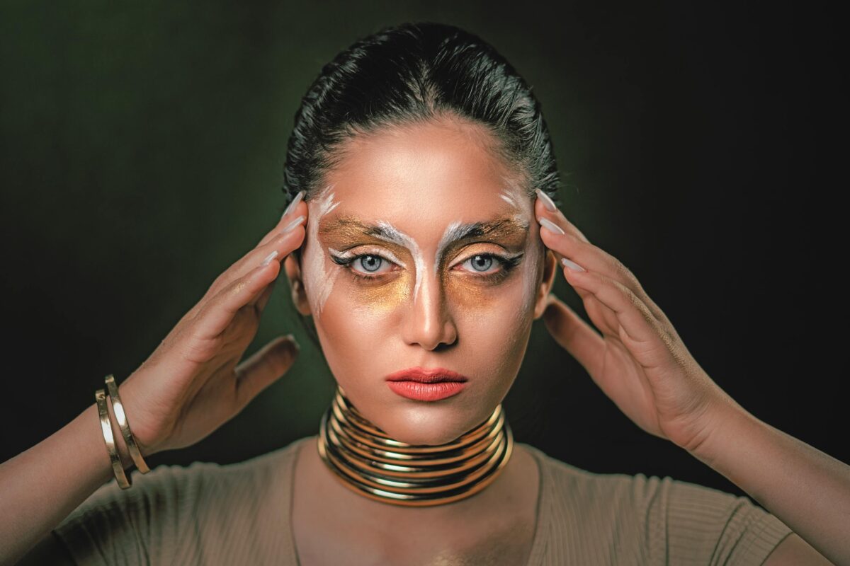 Close-up portrait of a woman with creative gold makeup and jewelry, conveying elegance and modern artistry.