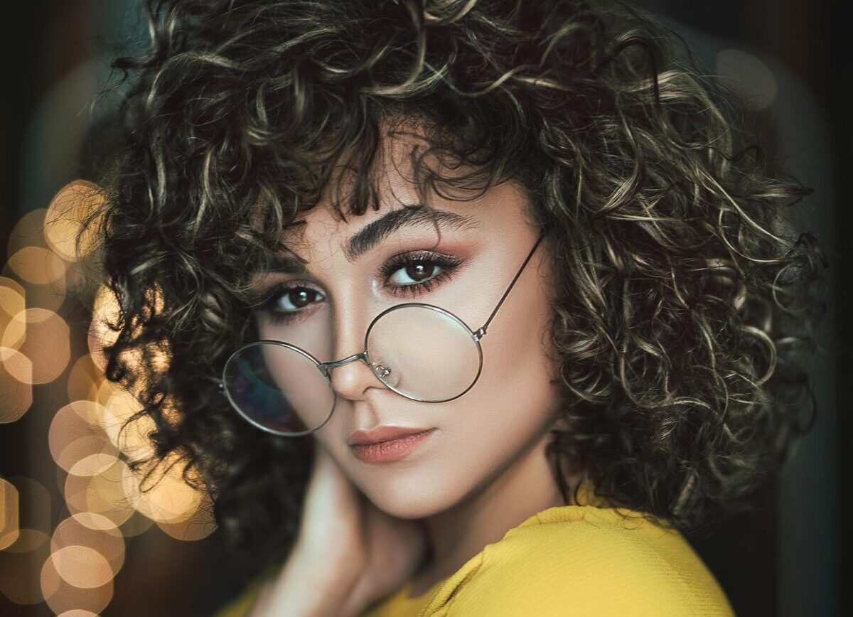 Stylish portrait of a woman with curly hair and eyeglasses in a vibrant setting.