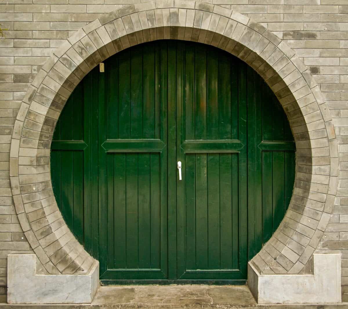A striking circular green door set in an arched brick wall showcasing vintage architectural design.