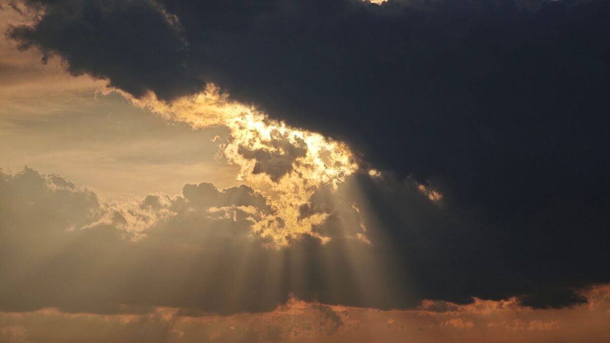 Sunlight rays penetrate dark clouds during sunset, creating a dramatic sky scene.