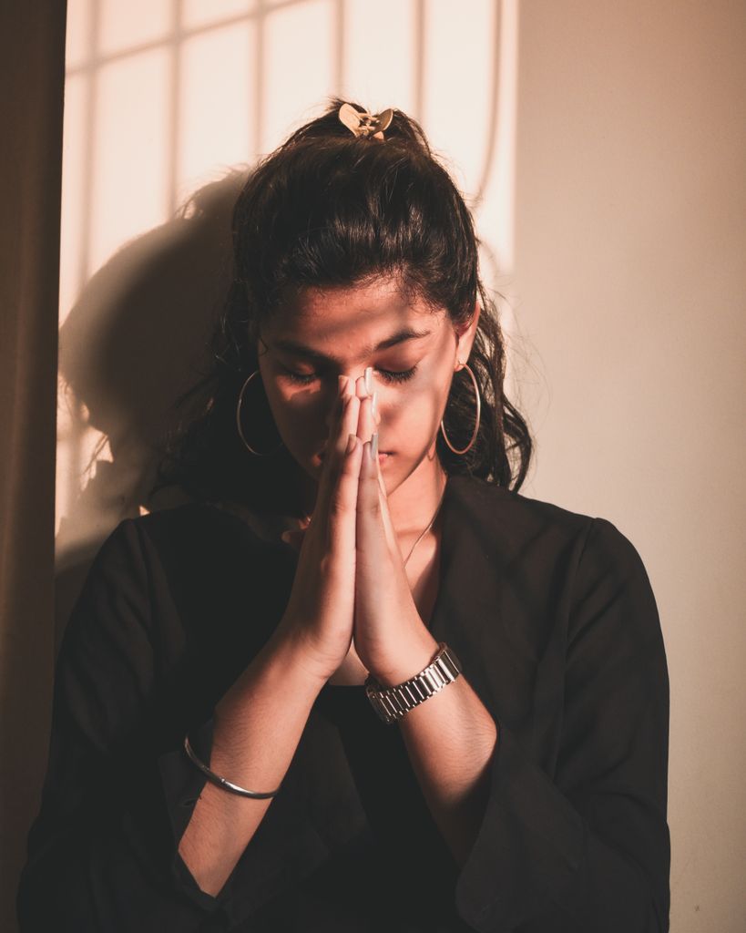 Young woman in a peaceful pose praying with eyes closed in warm sunlight indoors.